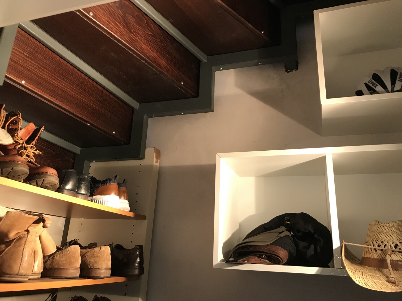 Shoe rack with sneakers and boots, next to white storage cubes with clothes and a hat.