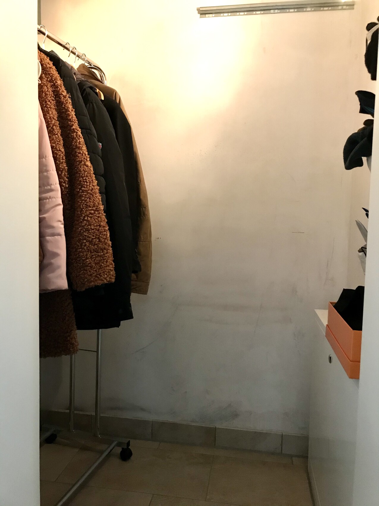 Wardrobe storage: coats hanging on the left, light wall in the middle, orange box on the right.