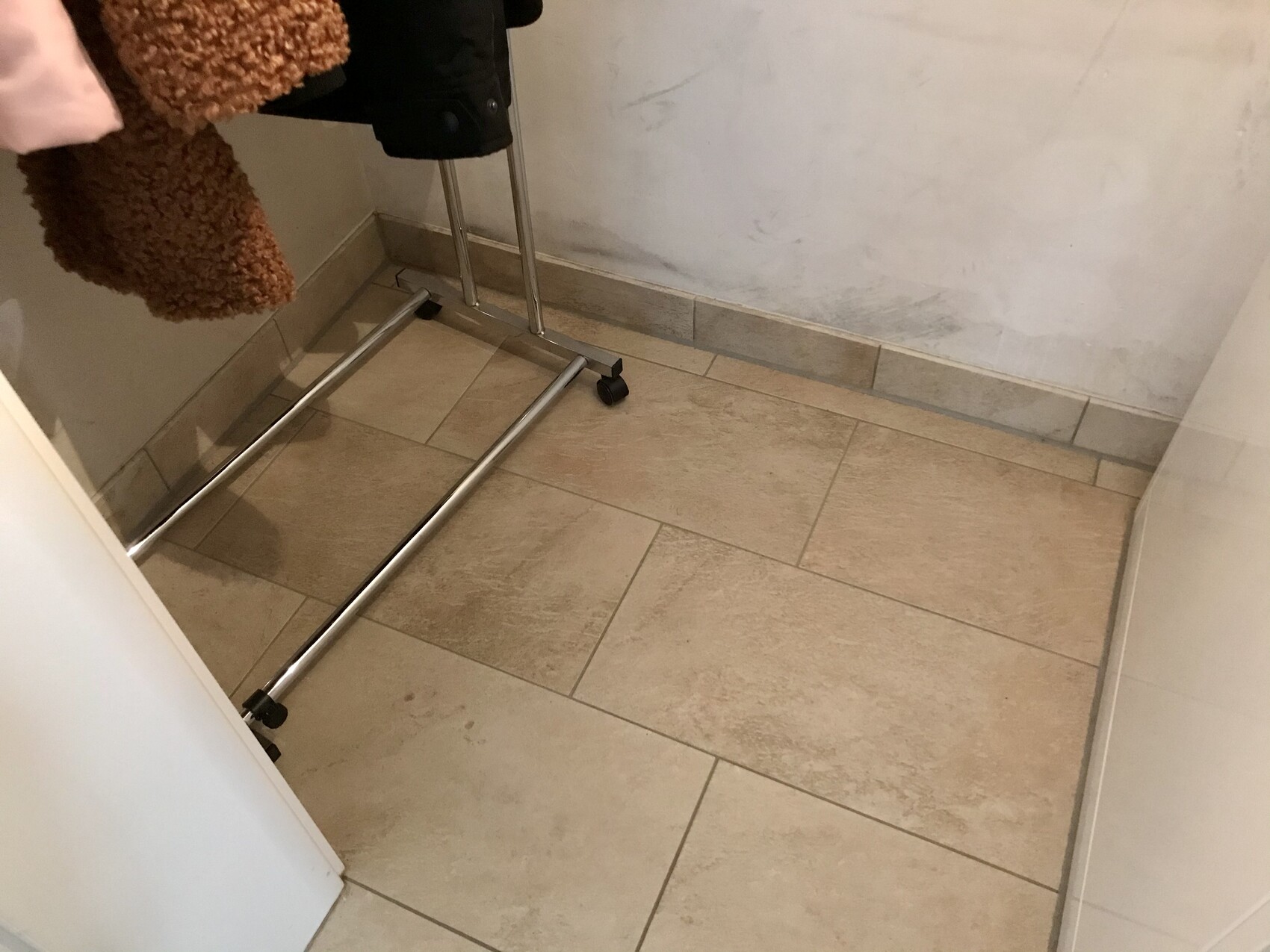 Metal clothes rack lying flat on beige tiles; coat hanging on it.