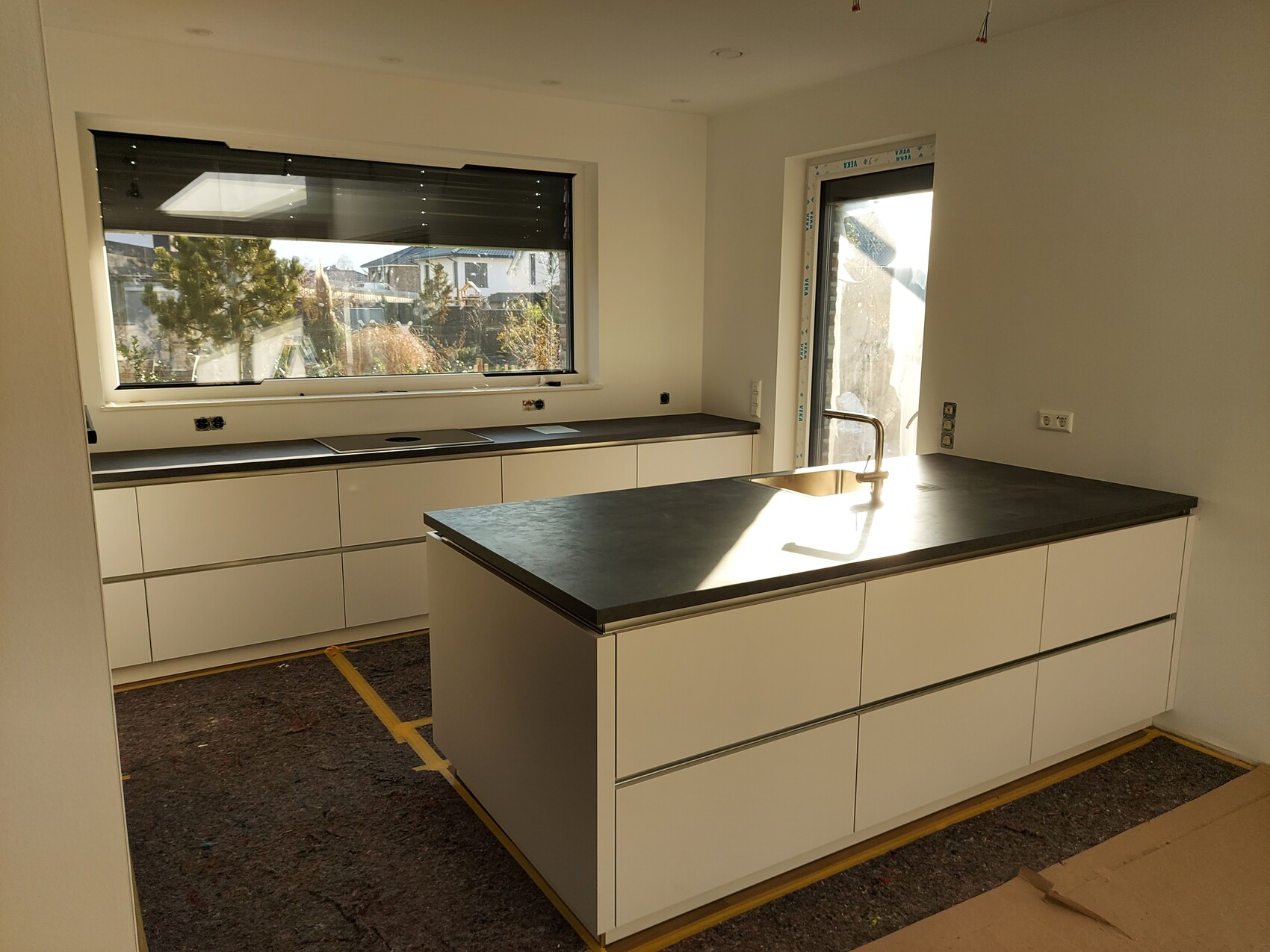 Weiße Küche mit Insel, dunkler Arbeitsplatte und Spüle in Bauphase.