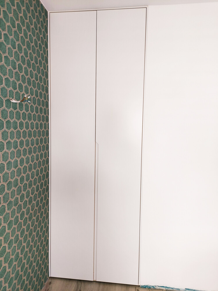 Bright white two-door cabinet in front of left green geometric wall, wooden floor.