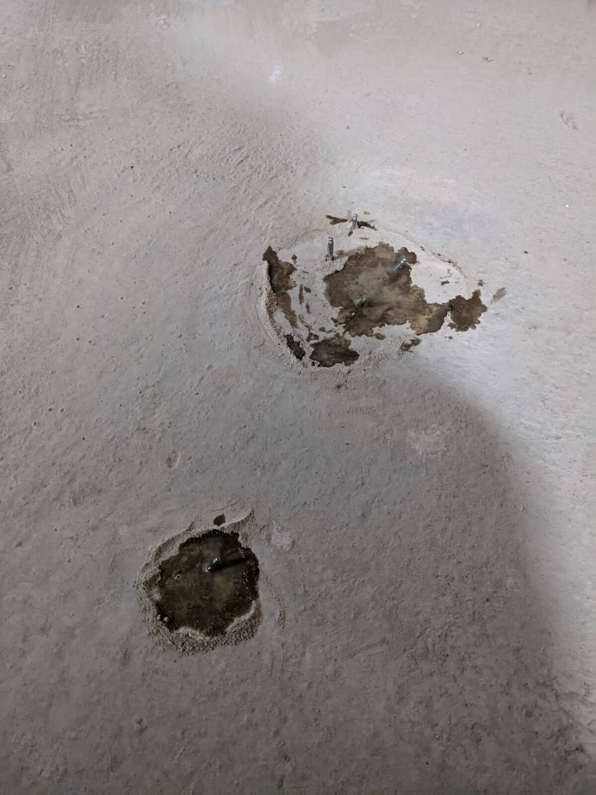 Betonboden mit drei runden Abplatzungen/Bohrlöchern, sichtbare Metallanker.