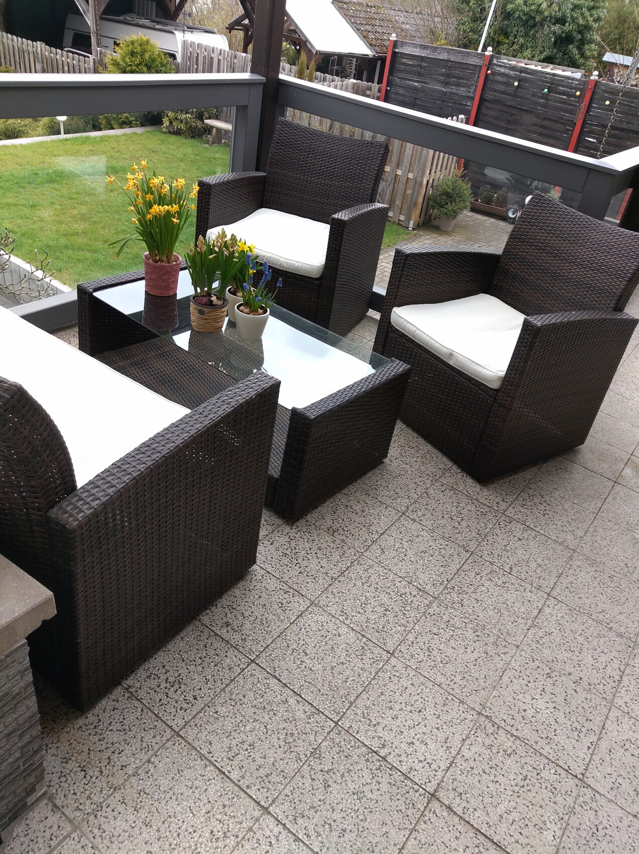 Garden terrace seating set made of dark brown rattan with glass table and potted plants.