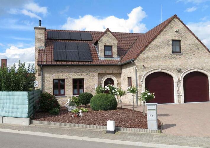 Two-story brick house with red roof tiles, solar panels, a well-kept front garden, and a double garage No. 63