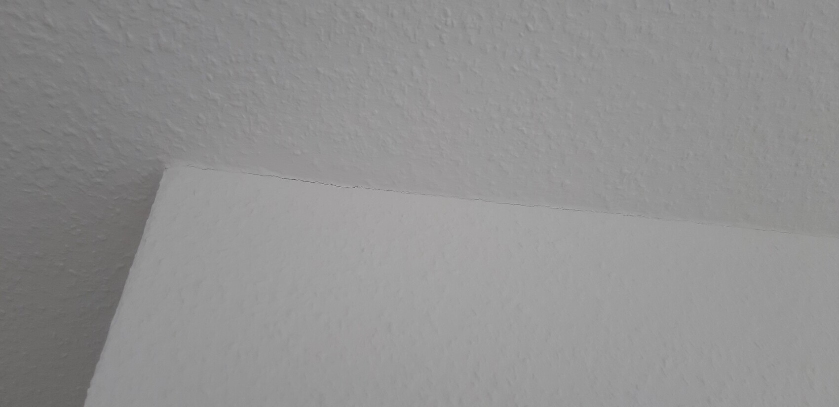 Close-up of the rough texture of a ceiling-wall joint with a fine crack line.