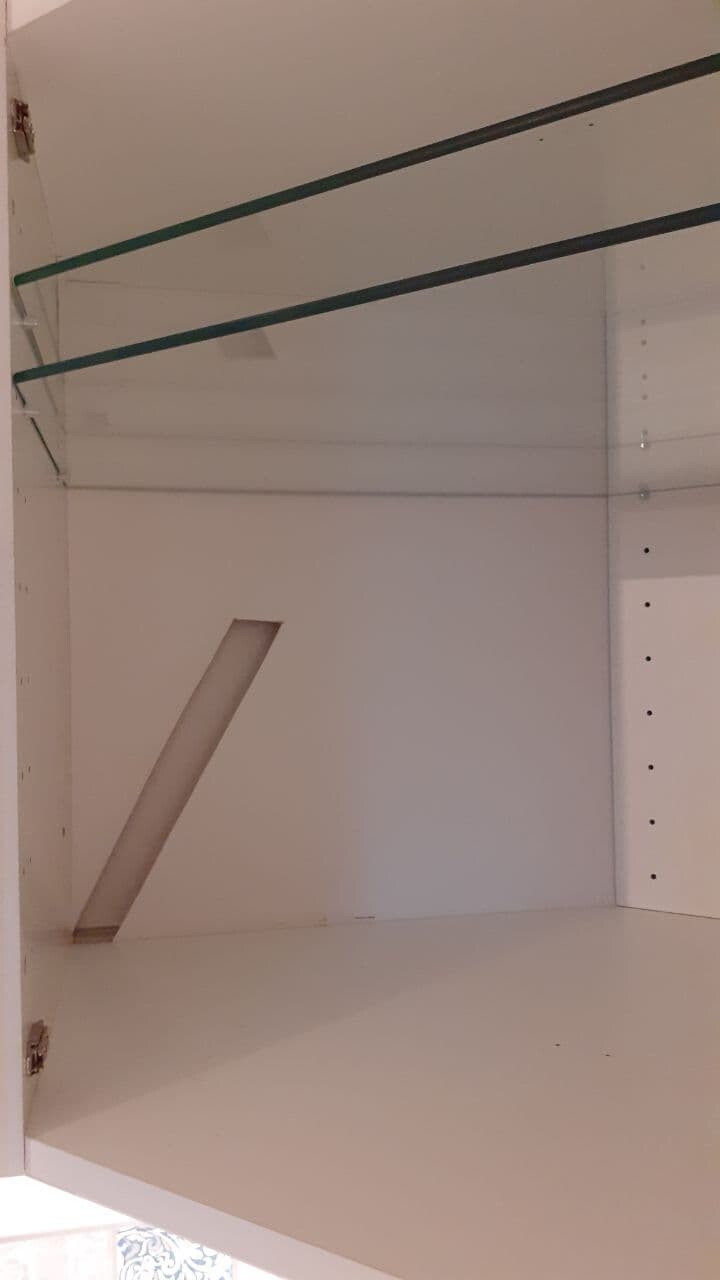 Open white cabinet with two dark rods; diagonal wooden board standing inside.