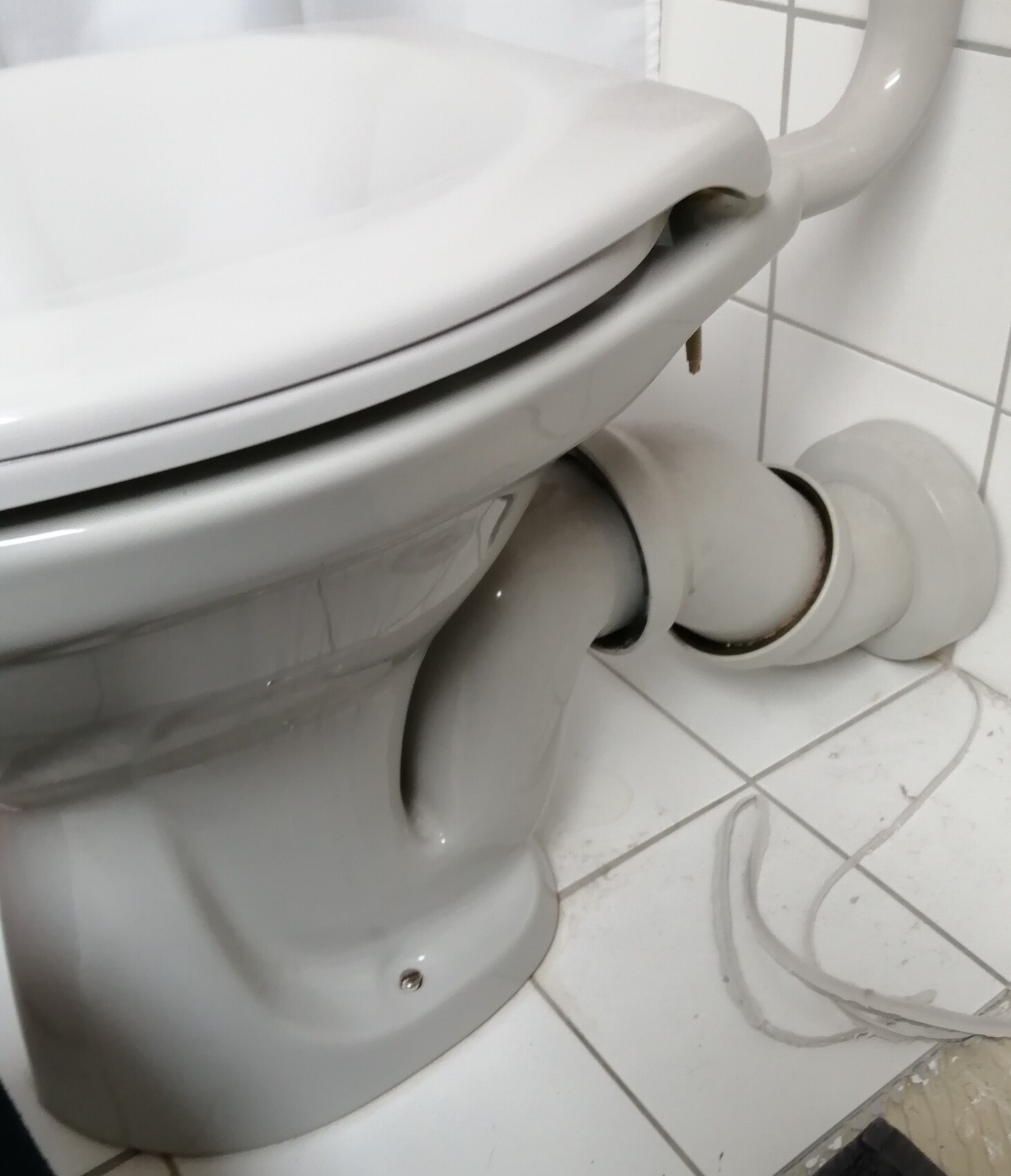 White toilet with closed lid, visible pipe connections on the floor.