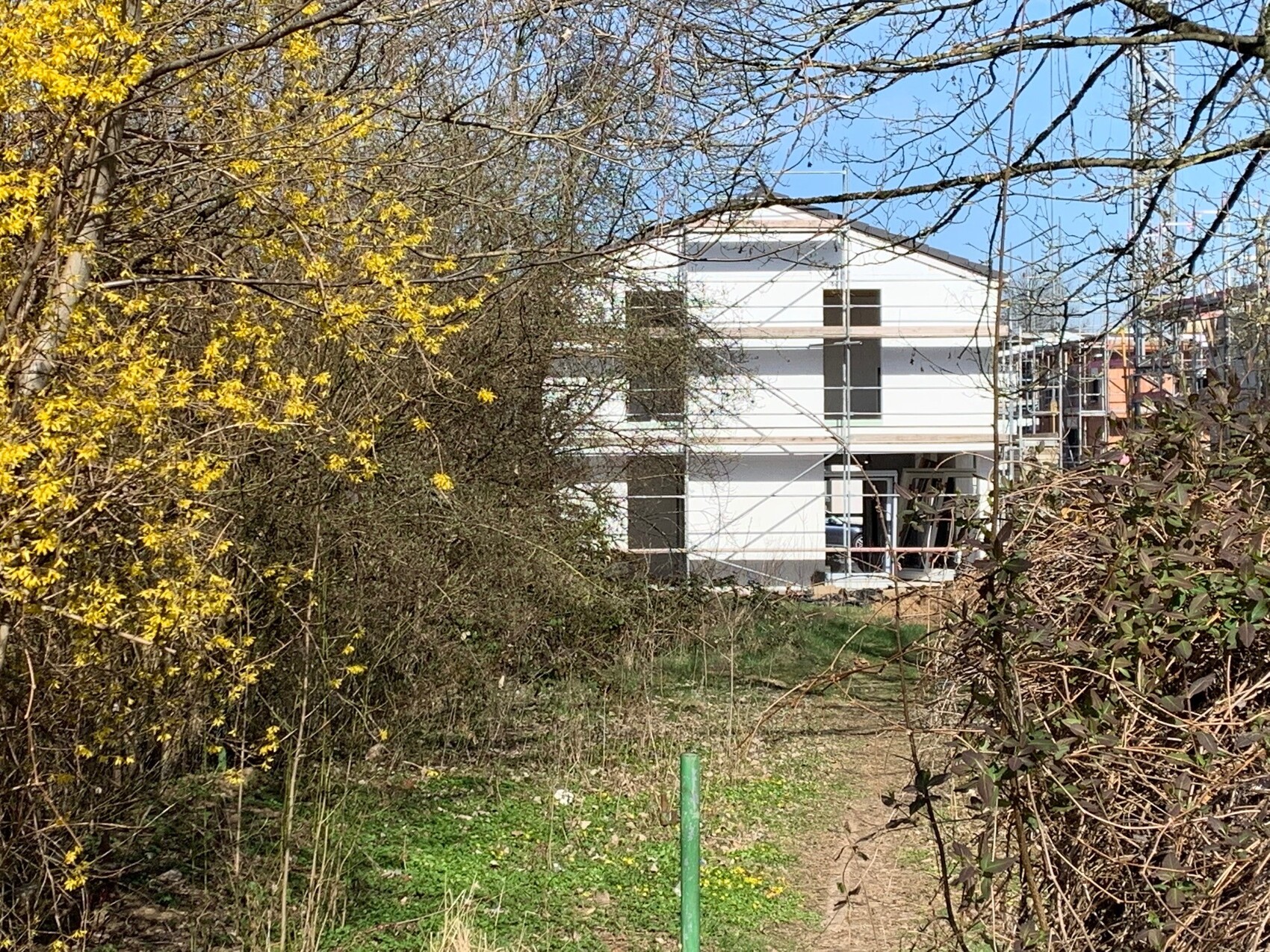 White two-story house under construction with scaffolding, surrounding terrain and trees in the foreground