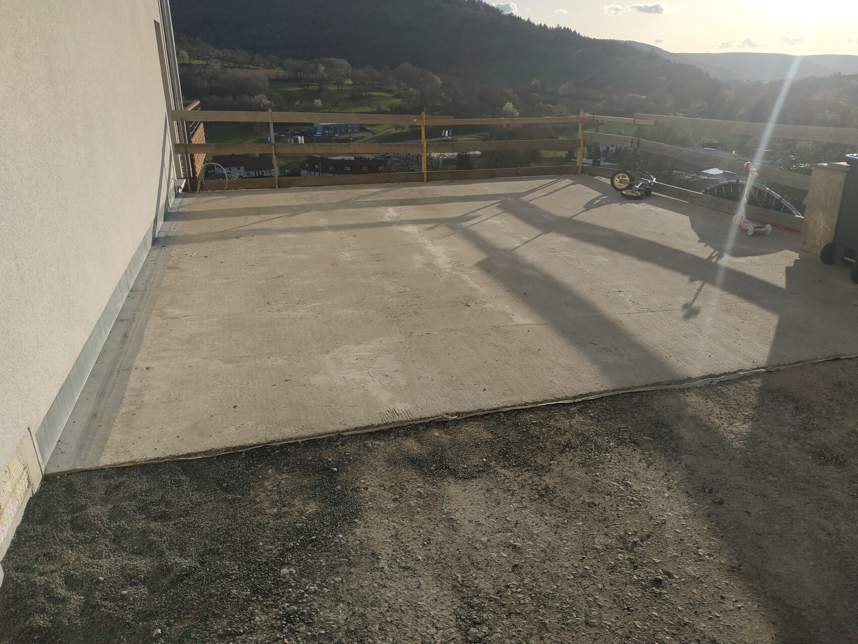 Terrace with wooden railing, view over hills and houses in the valley; toy vehicle lying at the edge.