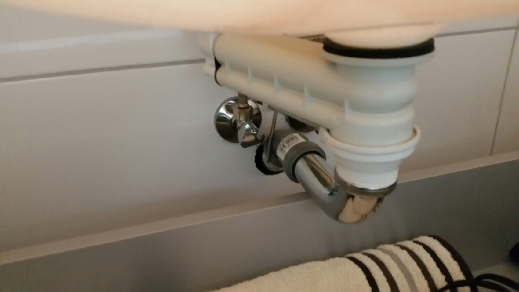 Visible trap drain pipe under the sink with shut-off valve and plastic parts.