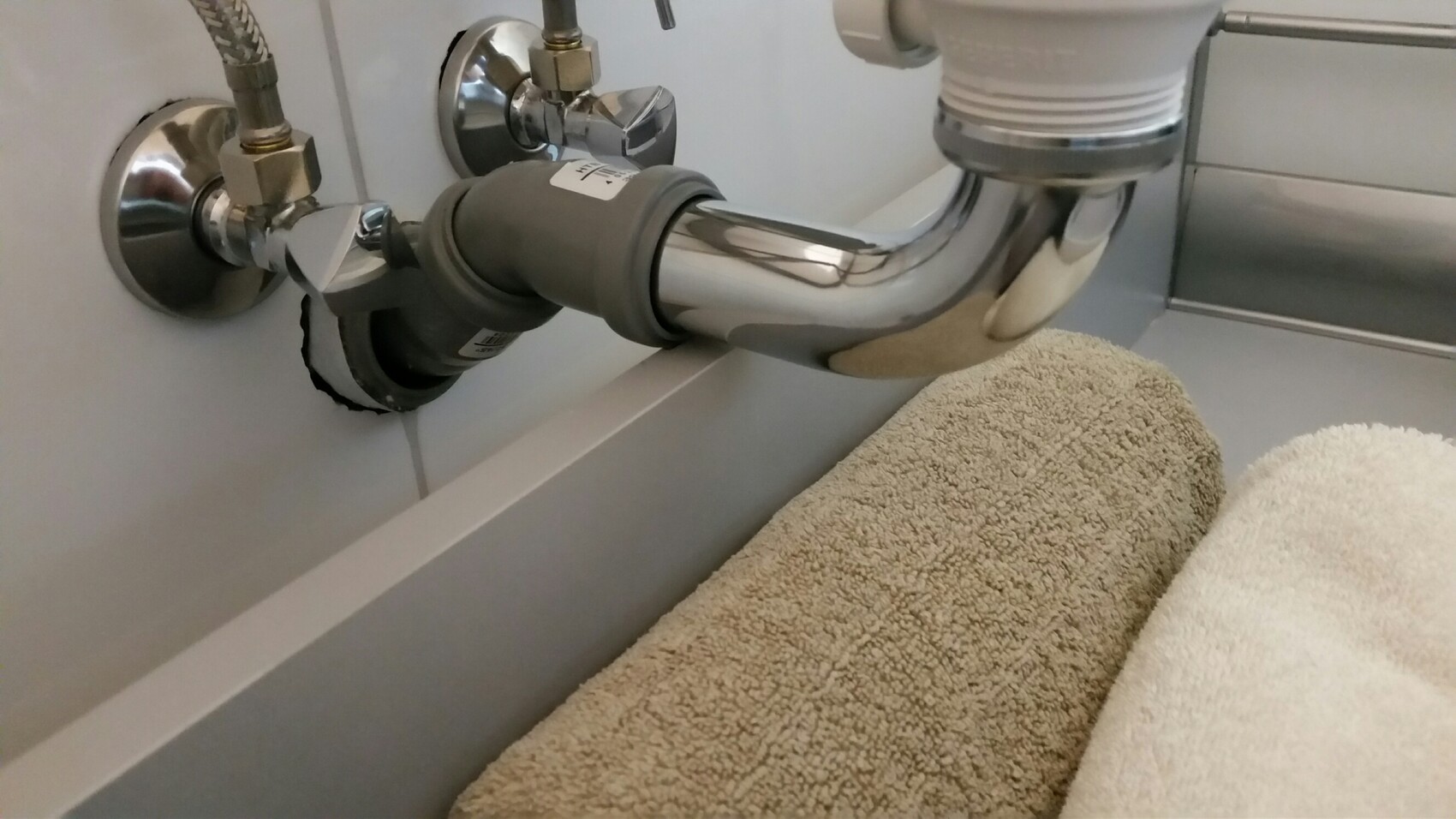 Chrome drain pipes, valves, and hoses under the kitchen sink; towels