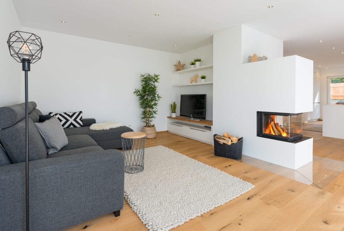 Modernes Wohnzimmer mit grauer Eckcouch, Kamin, TV, Pflanzen und hellem Holzboden