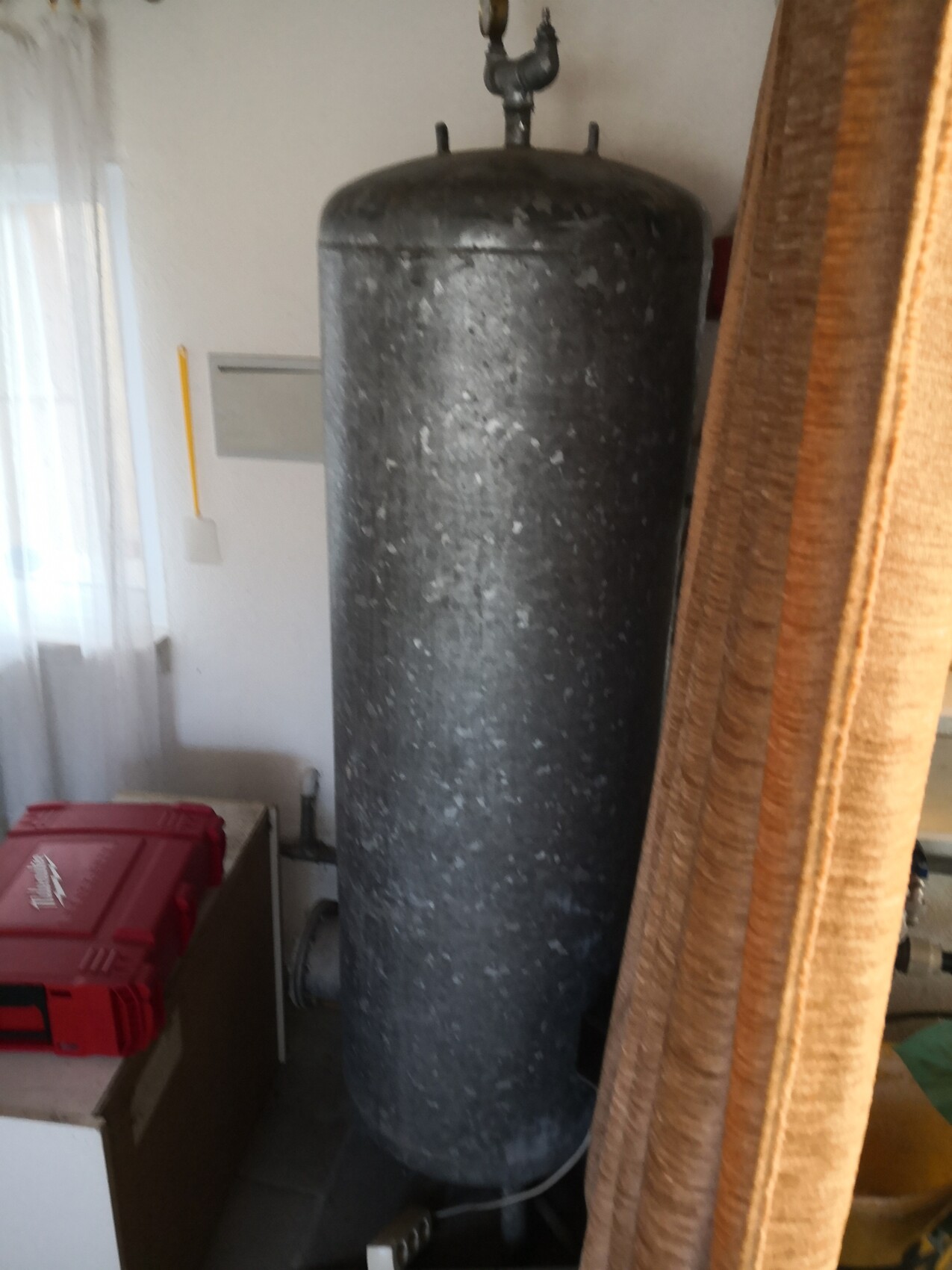 Large gray cylindrical tank with valve on top in the basement next to a curtain.