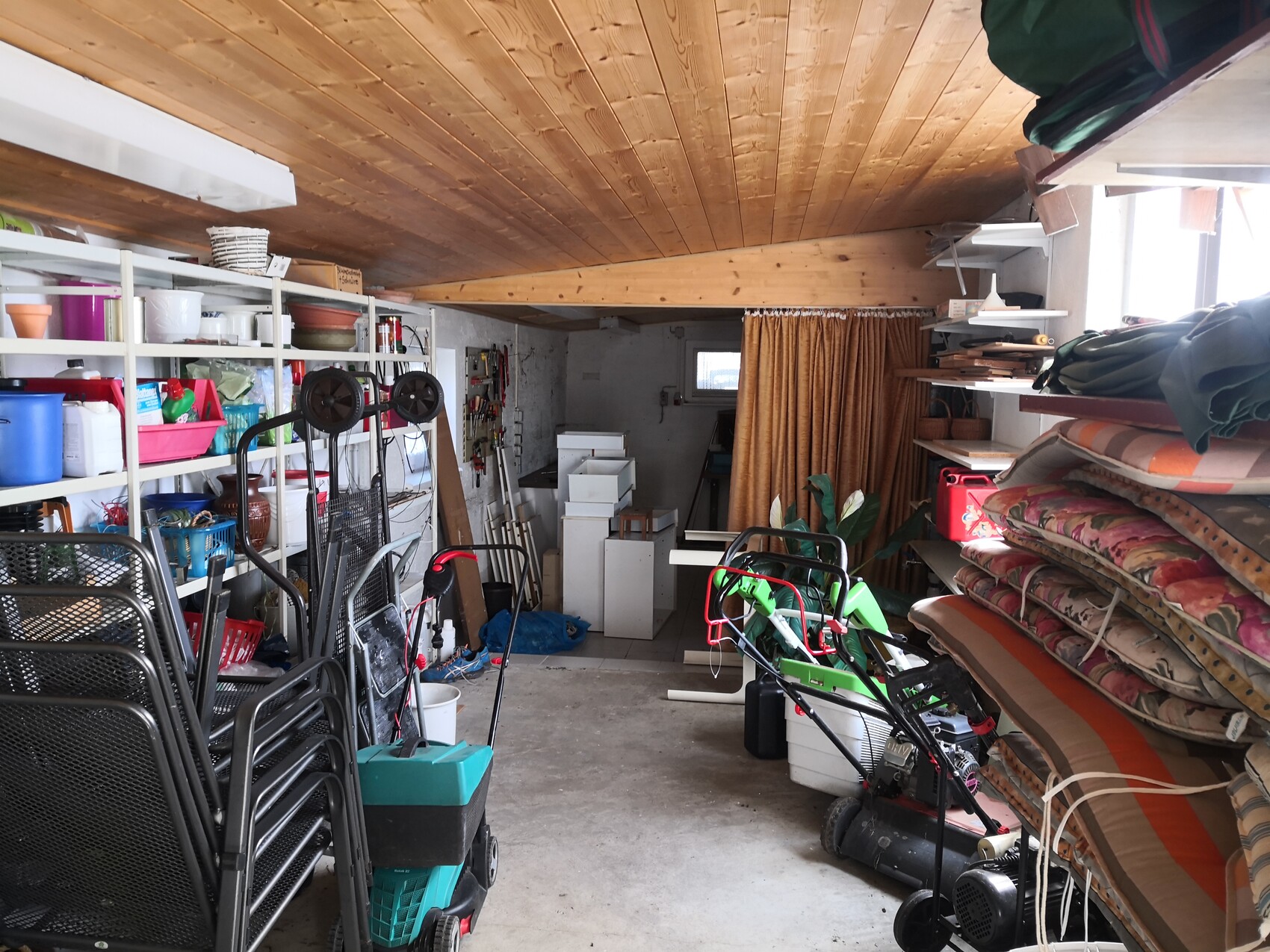 Storage room/basement: shelves with boxes, gardening tools, stacked chairs, mattresses.