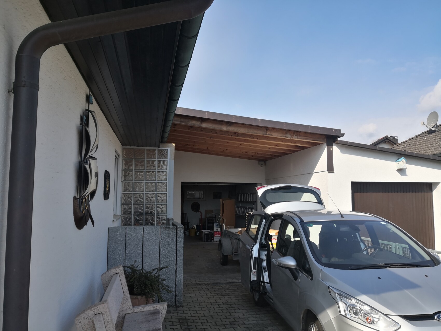 Silver van with open tailgate at a carport, in front courtyard with tools.