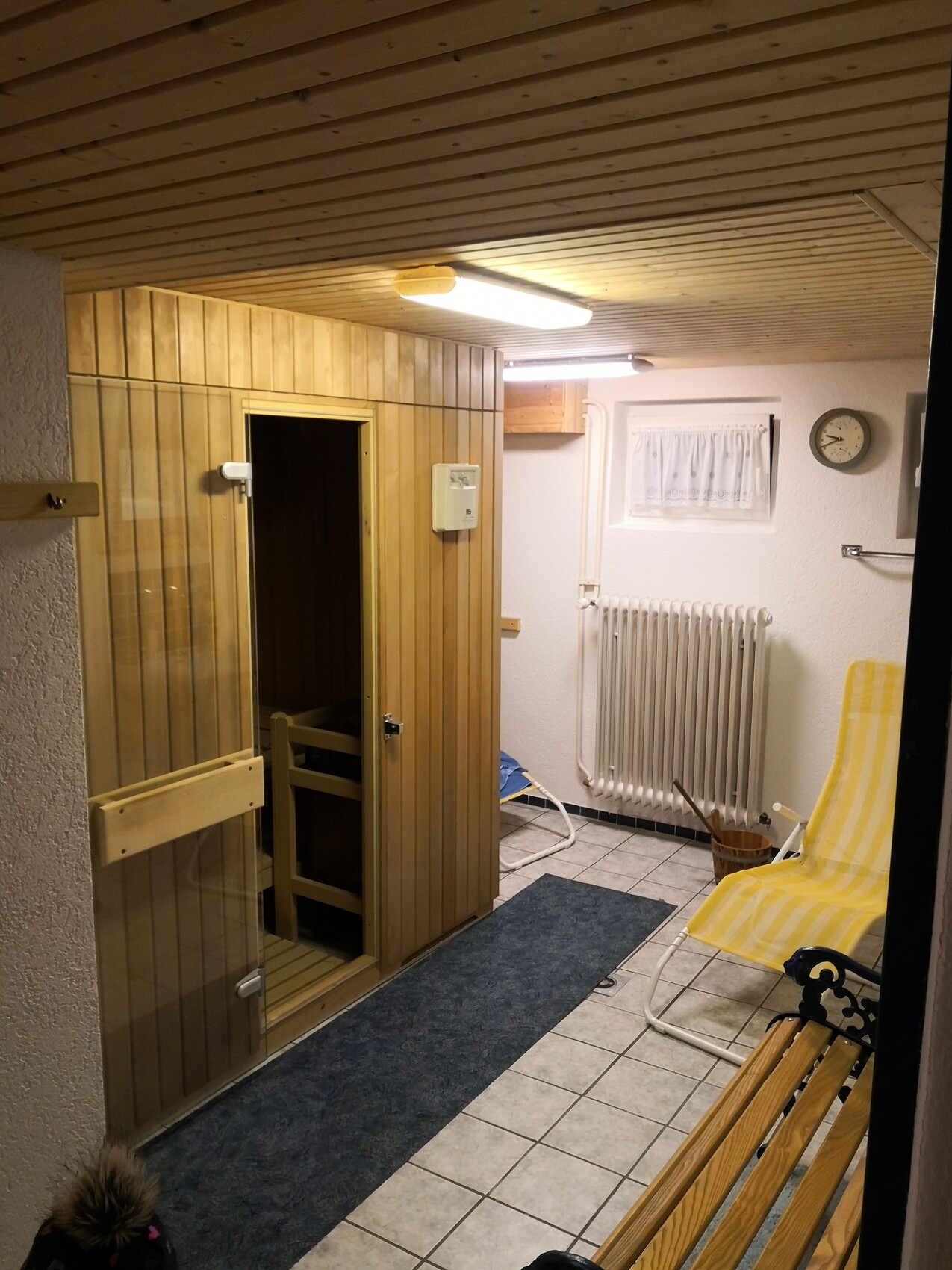Small sauna room with wooden wall sauna, glass door and yellow striped lounge chair.