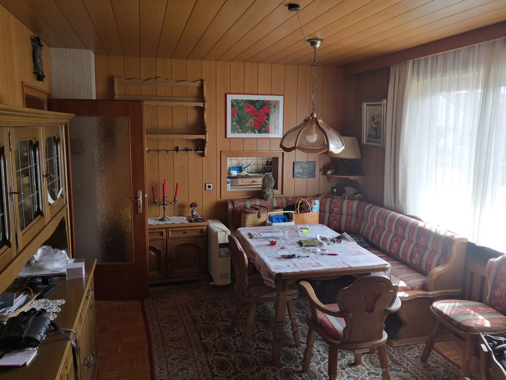 Wood-paneled dining area with dining table, corner bench, ceiling lamp and window front.
