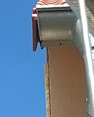 Close-up of roof edge with tiles and gutter under blue sky