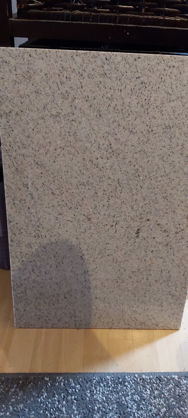 Large gray stone slab stands upright on wooden floor; fine pattern.