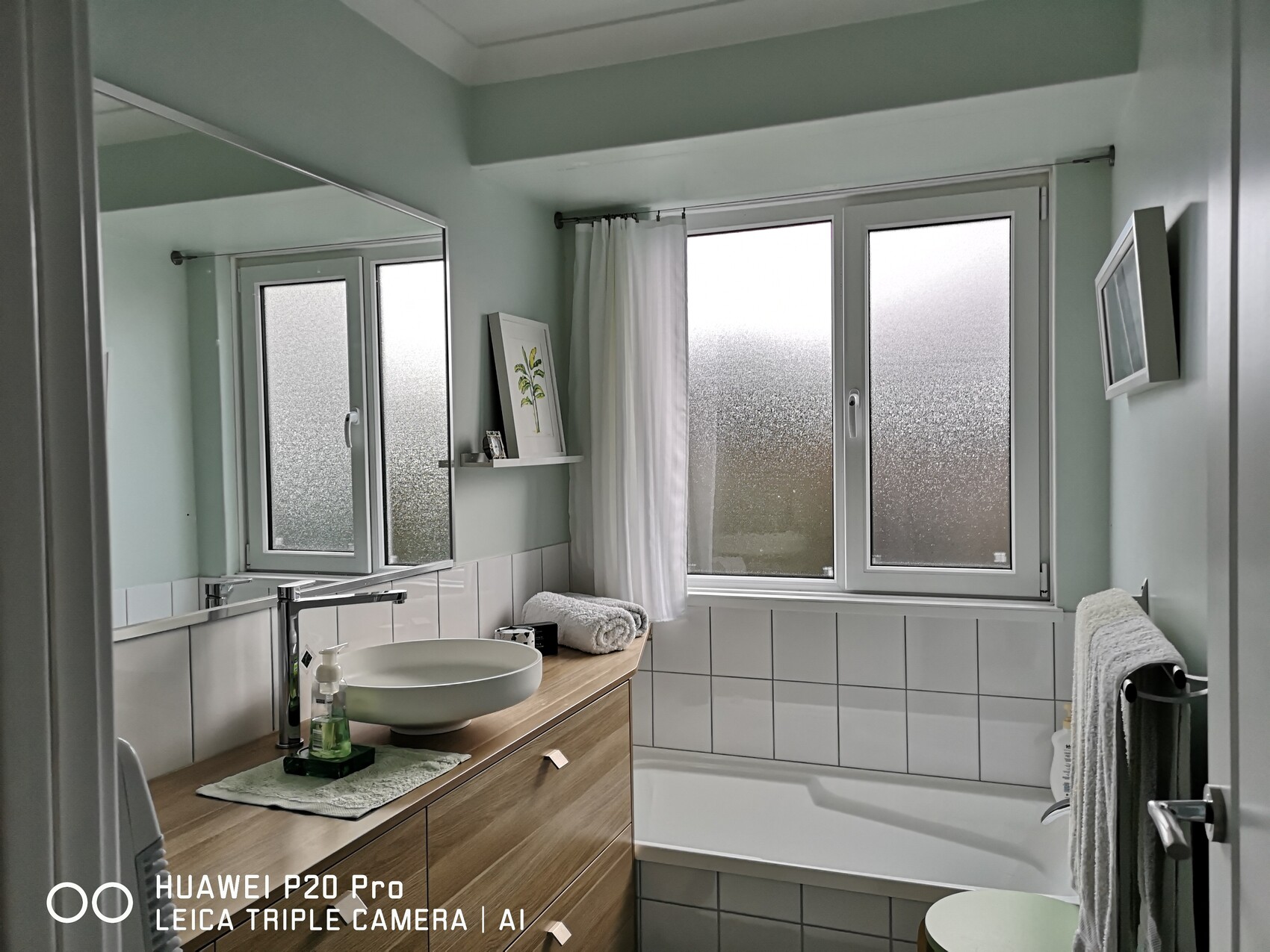 Bright bathroom with washbasin, wooden base cabinet, large mirror, and frosted glass windows