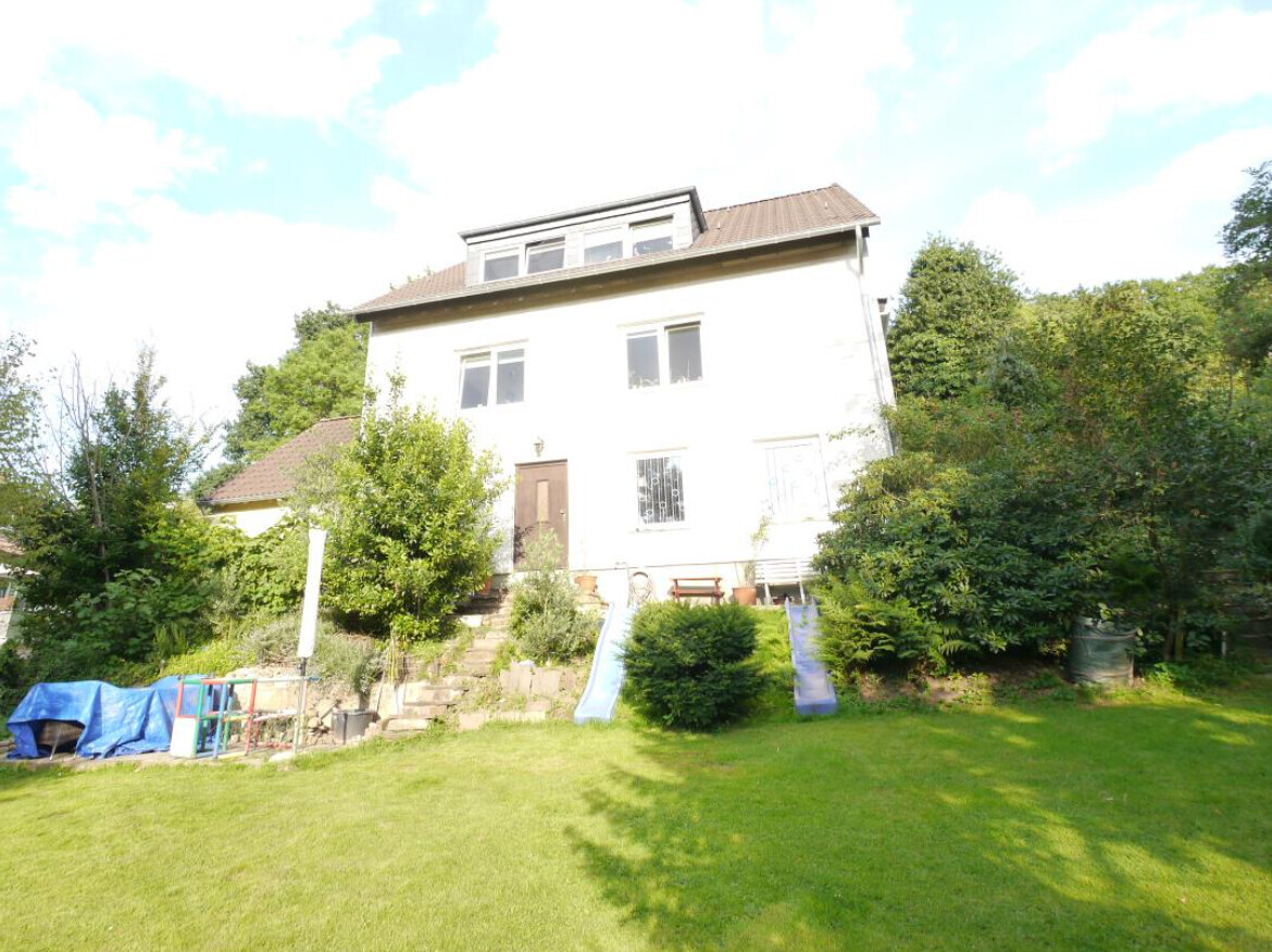 White two-story house with garden; two slides and playground equipment in the front yard.