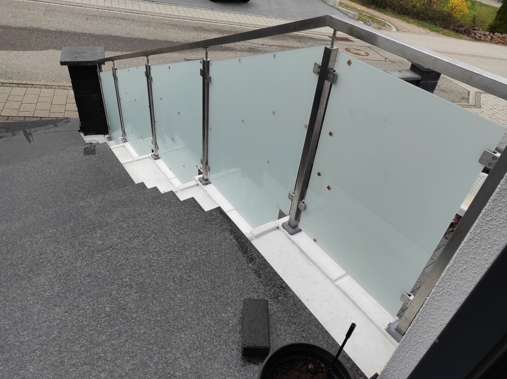 Outdoor area of a staircase with glass railing made of glass panels and metal posts, view towards the street.