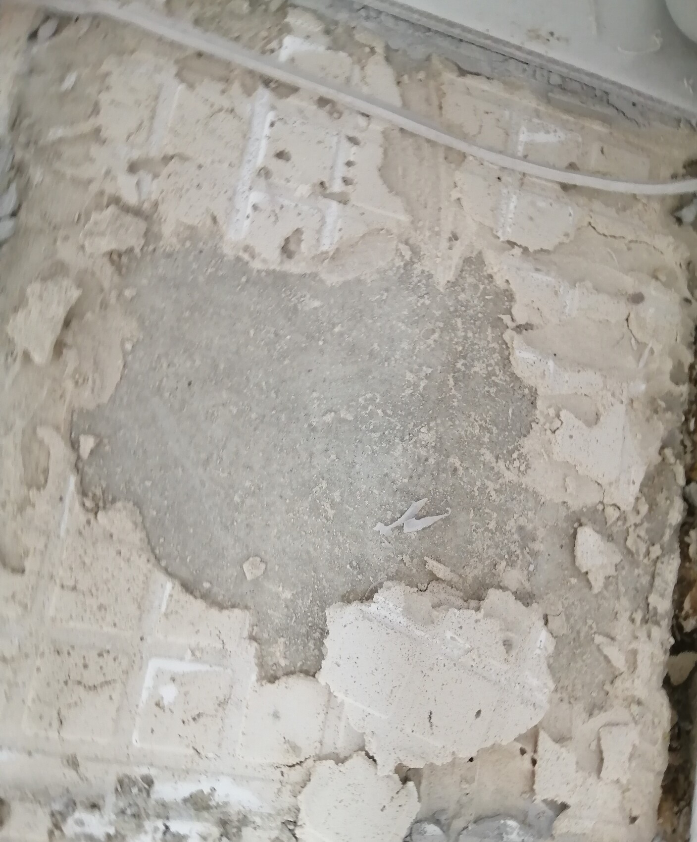 Rough wall section with flaking plaster, exposed masonry and a cable line.