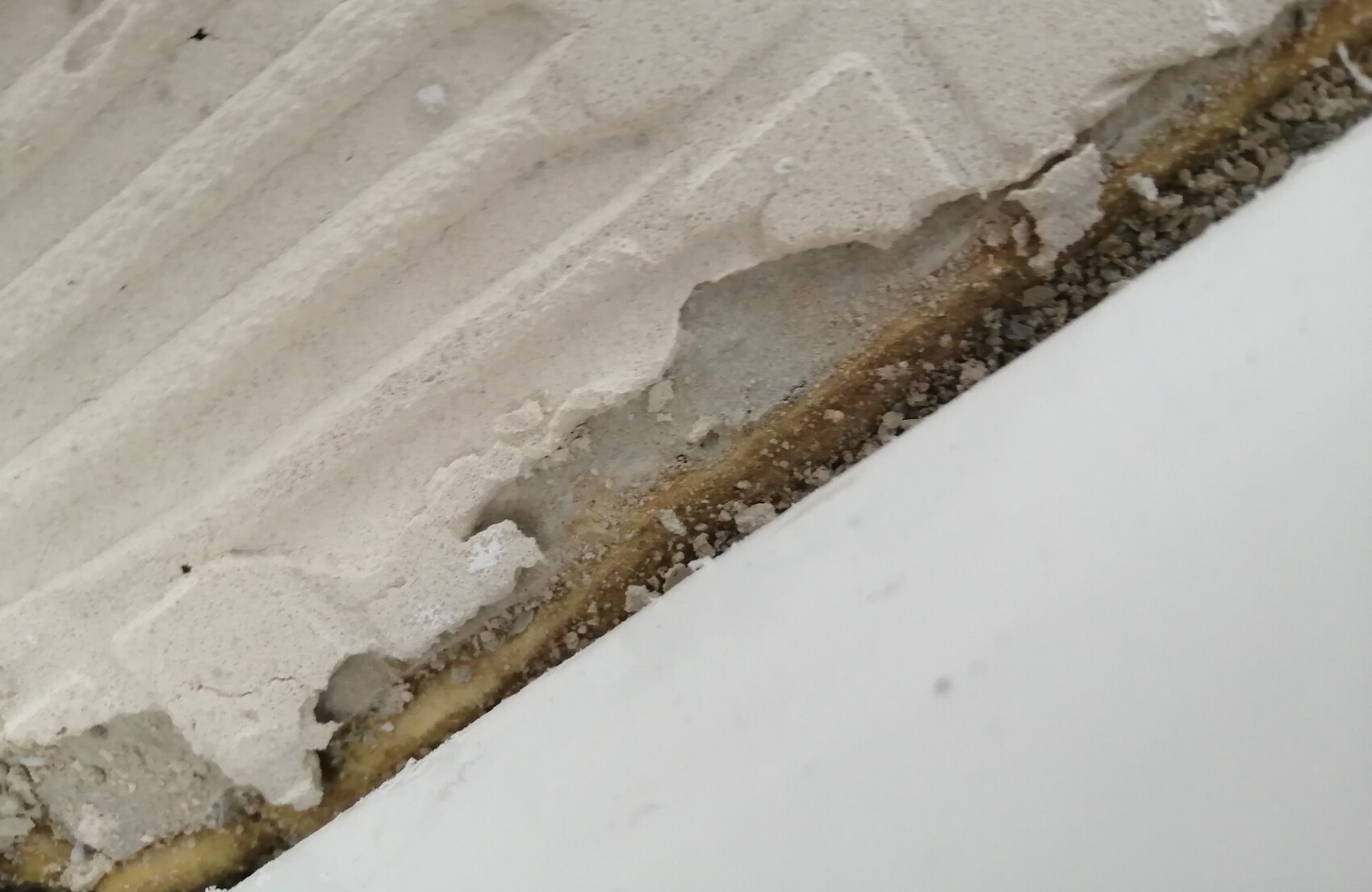 Close-up of crumbling plaster on a wall with cracks, dust and gravel; white area at bottom right