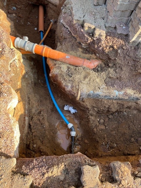 Excavation pit with orange main pipe and blue supply line, mud and water.