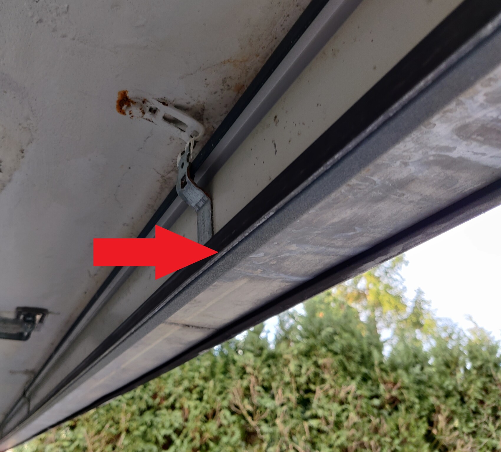 Rusty metal bracket on garage door track; visible seal, outdoor area with trees.