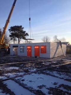 Shell construction site with crane lifting wall elements, smallest building with orange doors in the snow