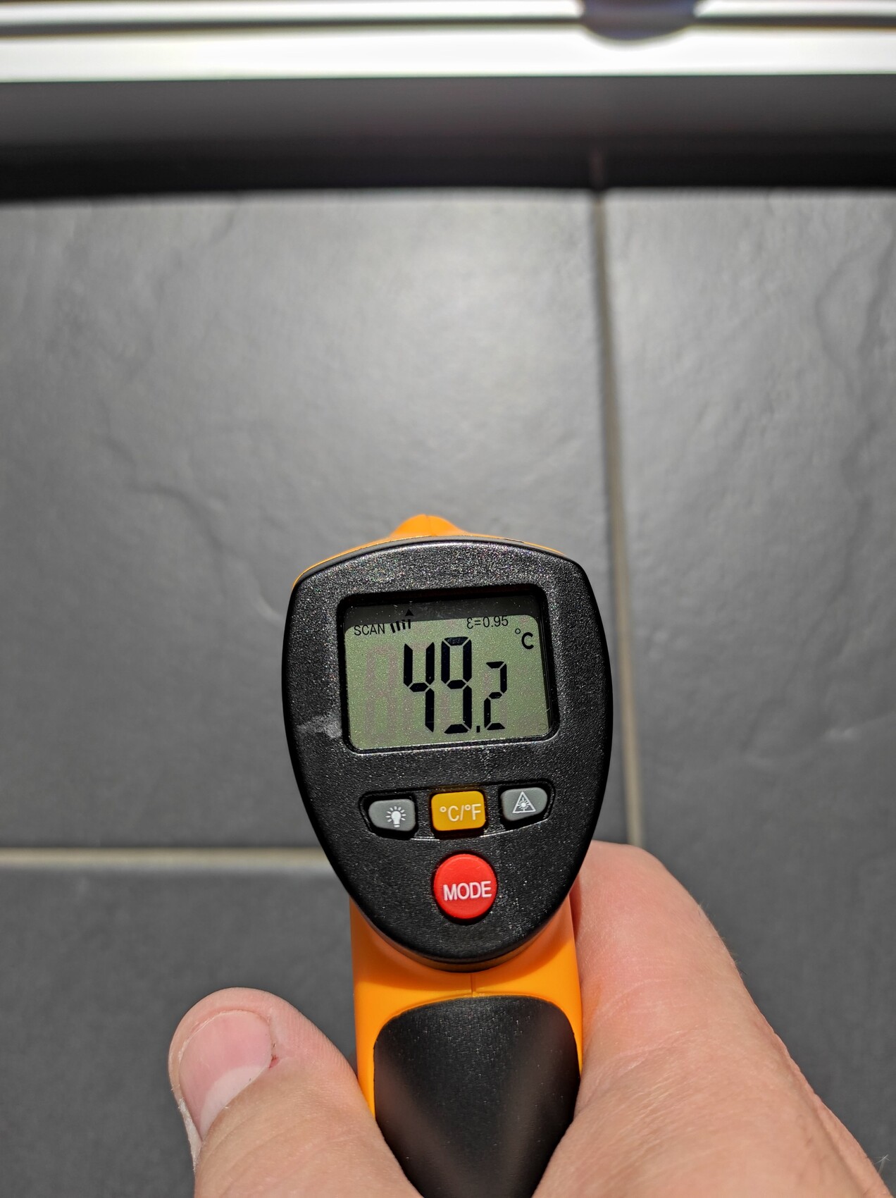 Close-up of an infrared thermometer showing 49.2 °C on a metal surface