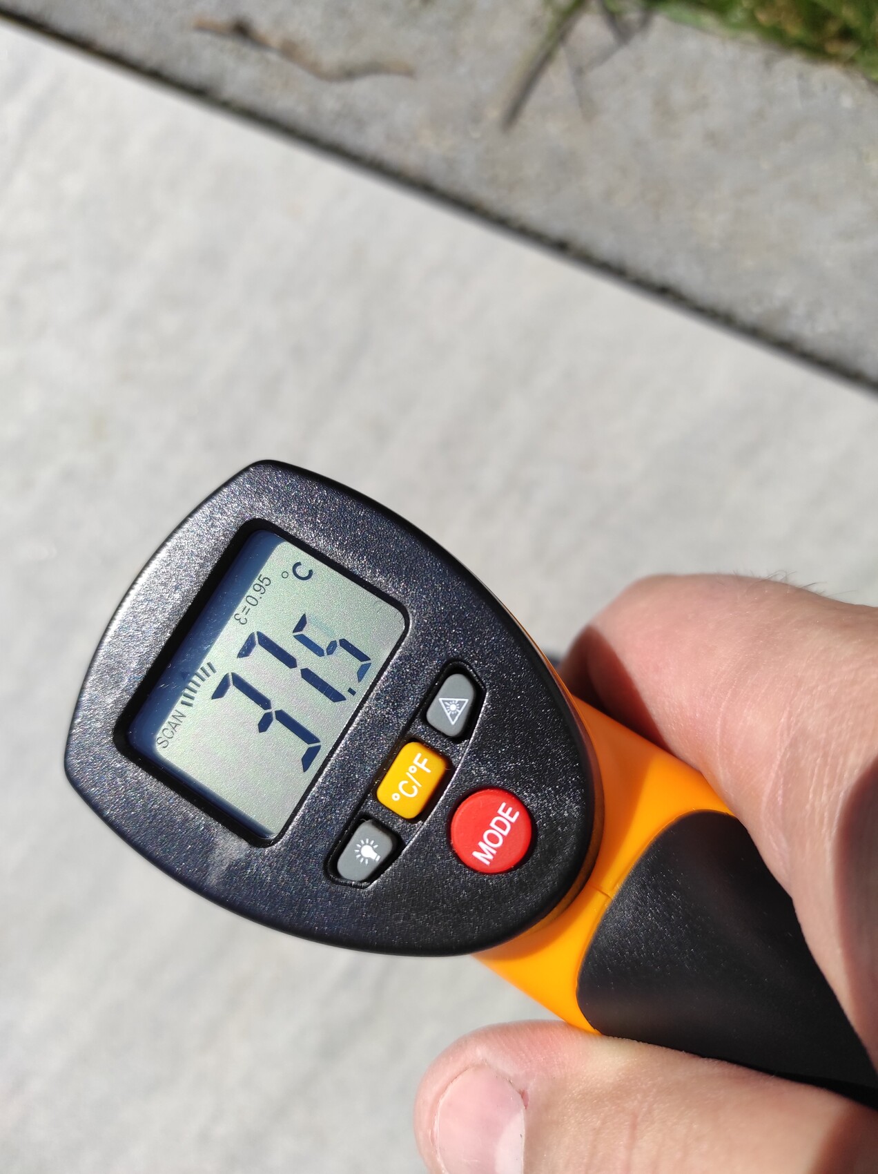 Close-up of an orange-black infrared thermometer showing 27.7 °C held by hand.
