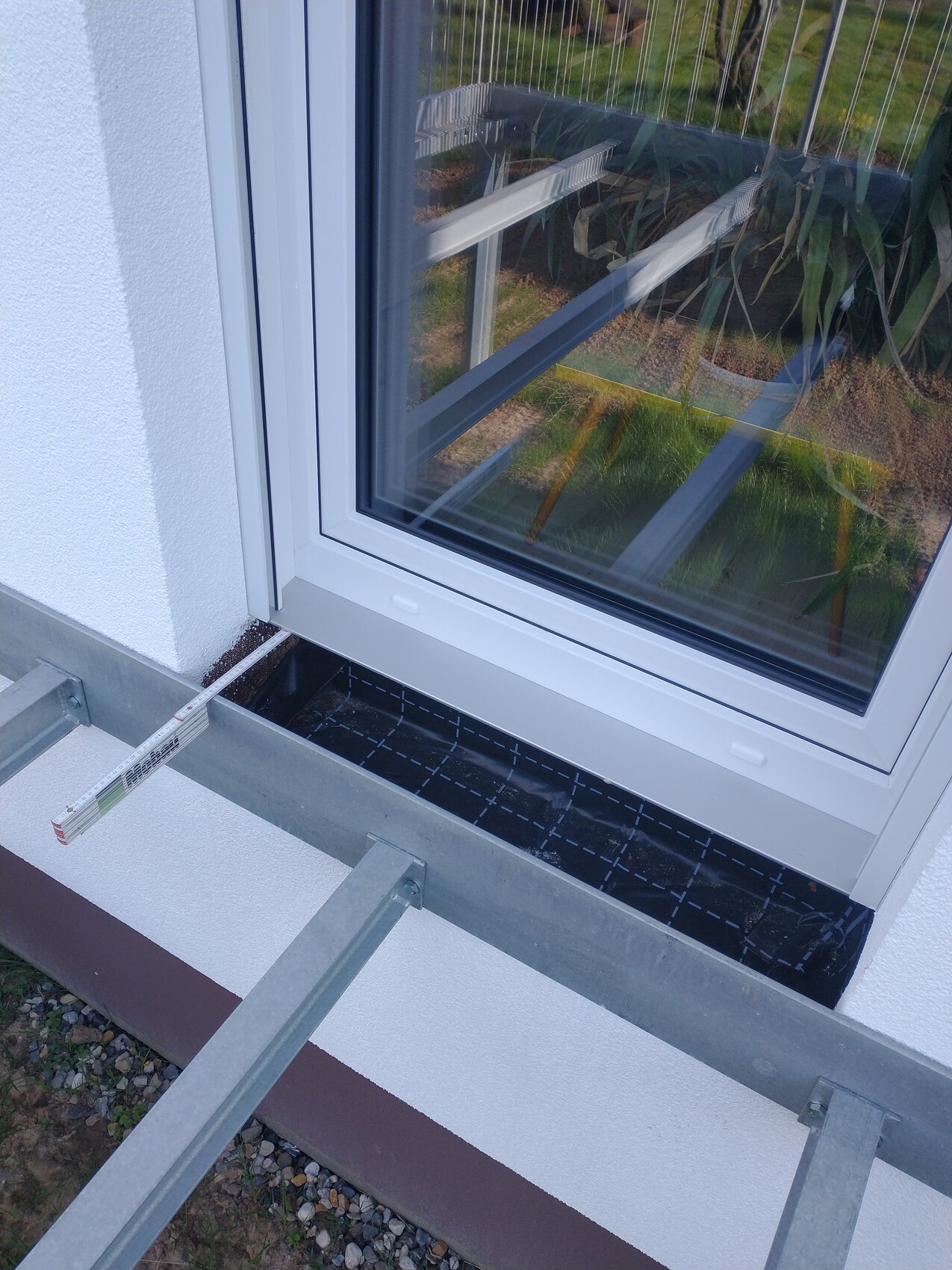 Außenfenster in weißer Fassade; Baugerüstteile und eine Wasserwaage liegen davor.