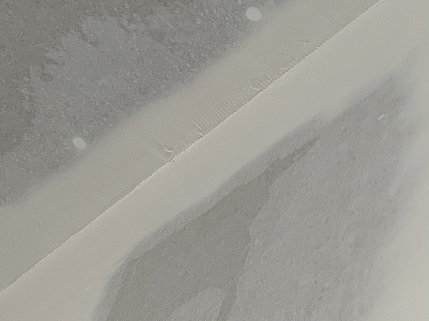 Close-up of a white edging strip on coarse gray substrate, arranged diagonally.