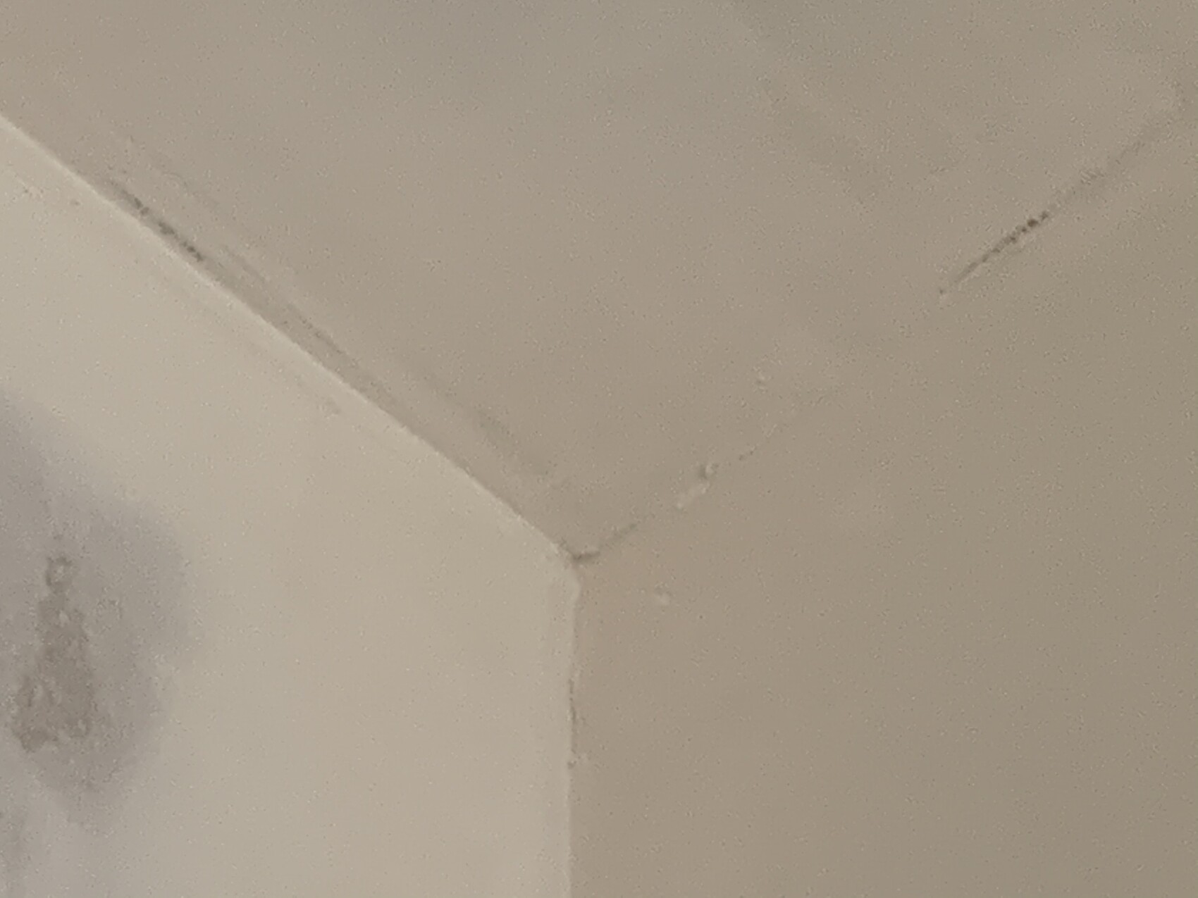 White ceiling and wall corner with crack lines, stain at lower left