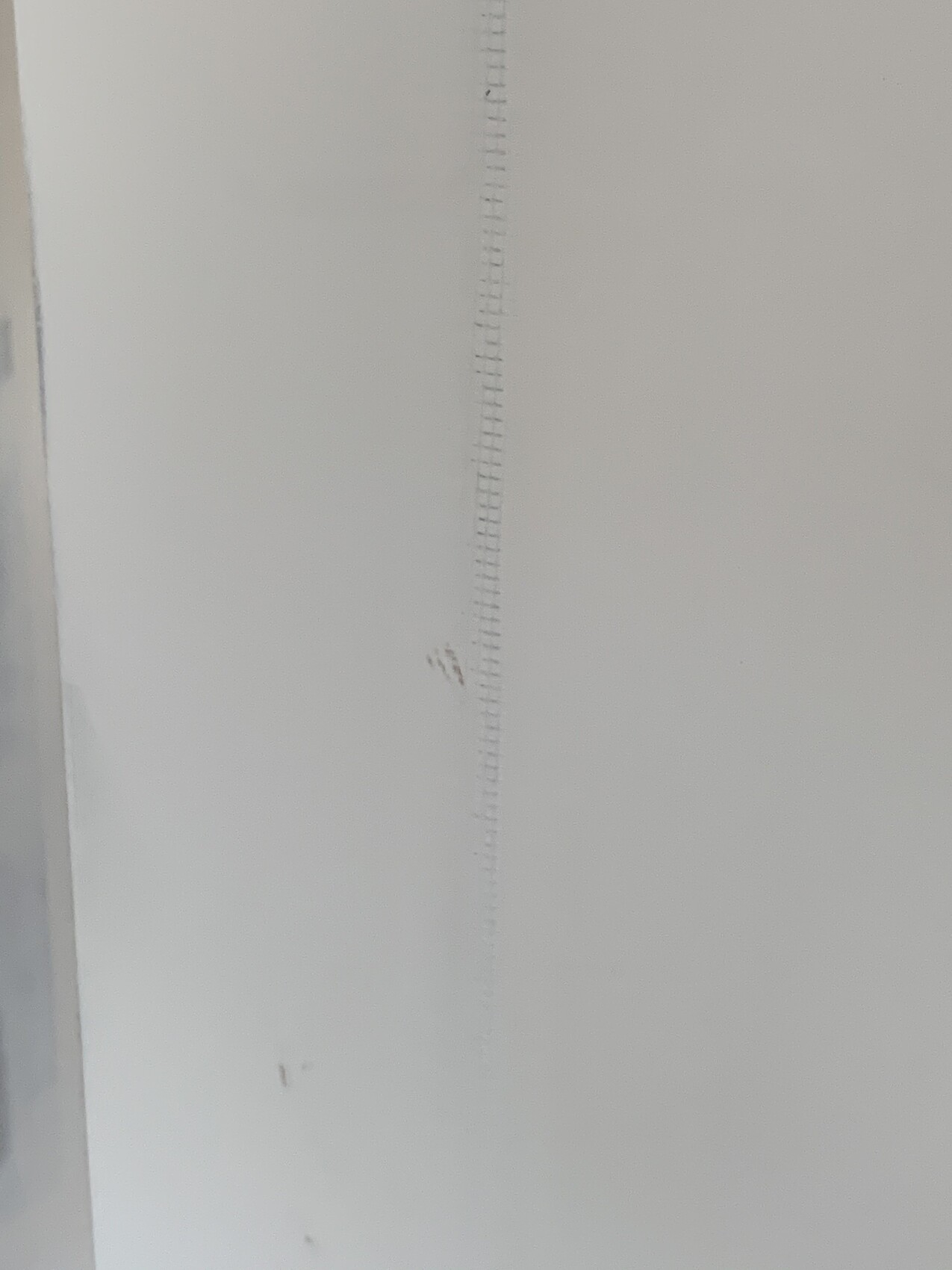 Vertical measuring rod with fine markings on white wall.