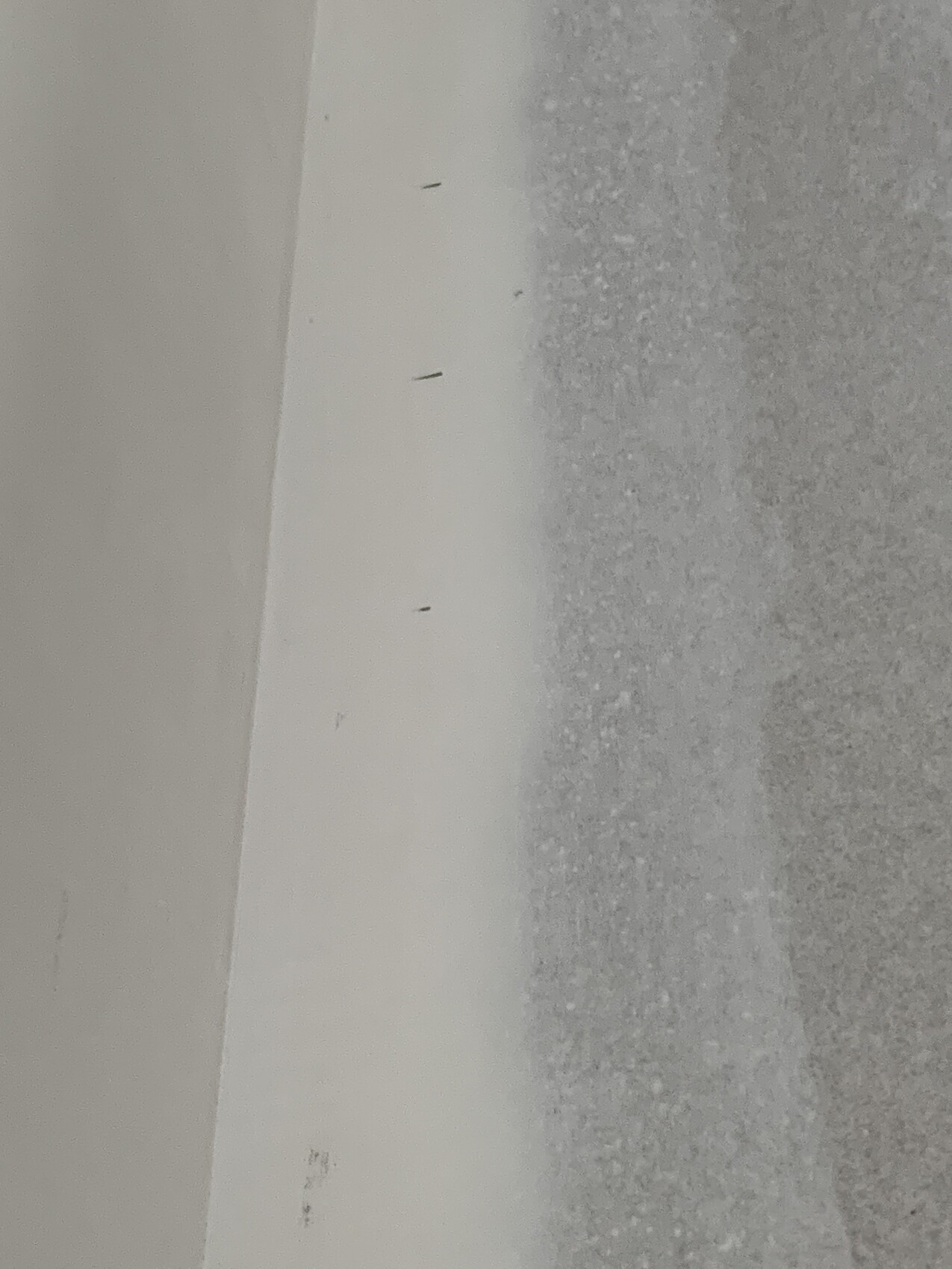 White wall edge with small dark nails; right side rough gray substrate.