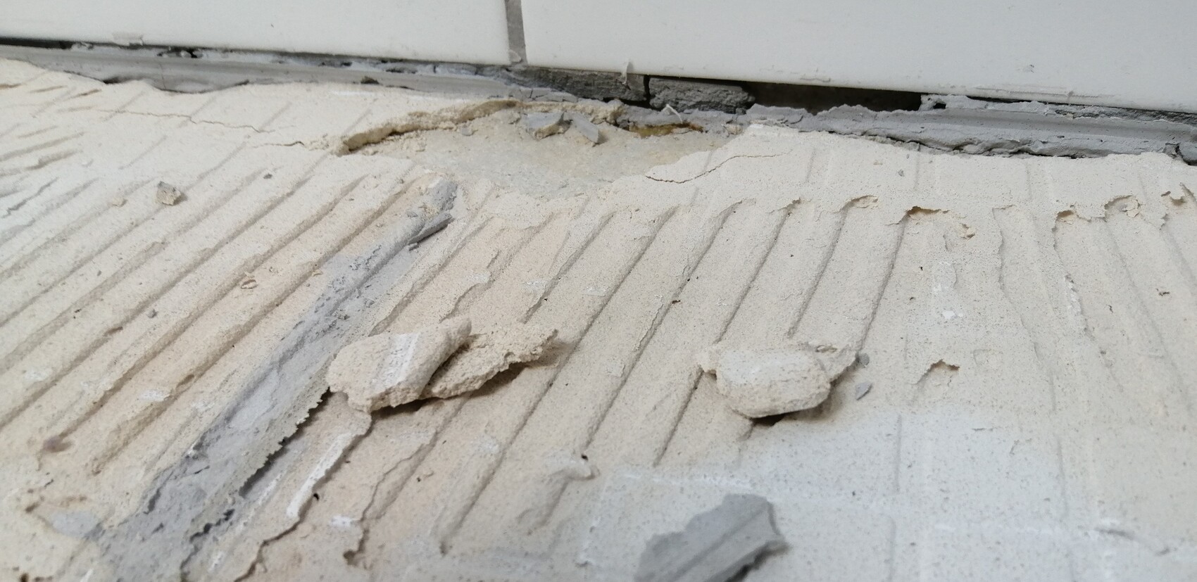 Broken plaster pieces on a ribbed screed floor in front of a door edge.
