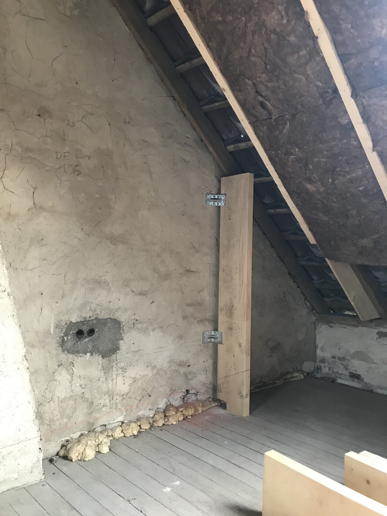 Unfinished attic with visible wooden beams, rough walls and insulation in the roof area.