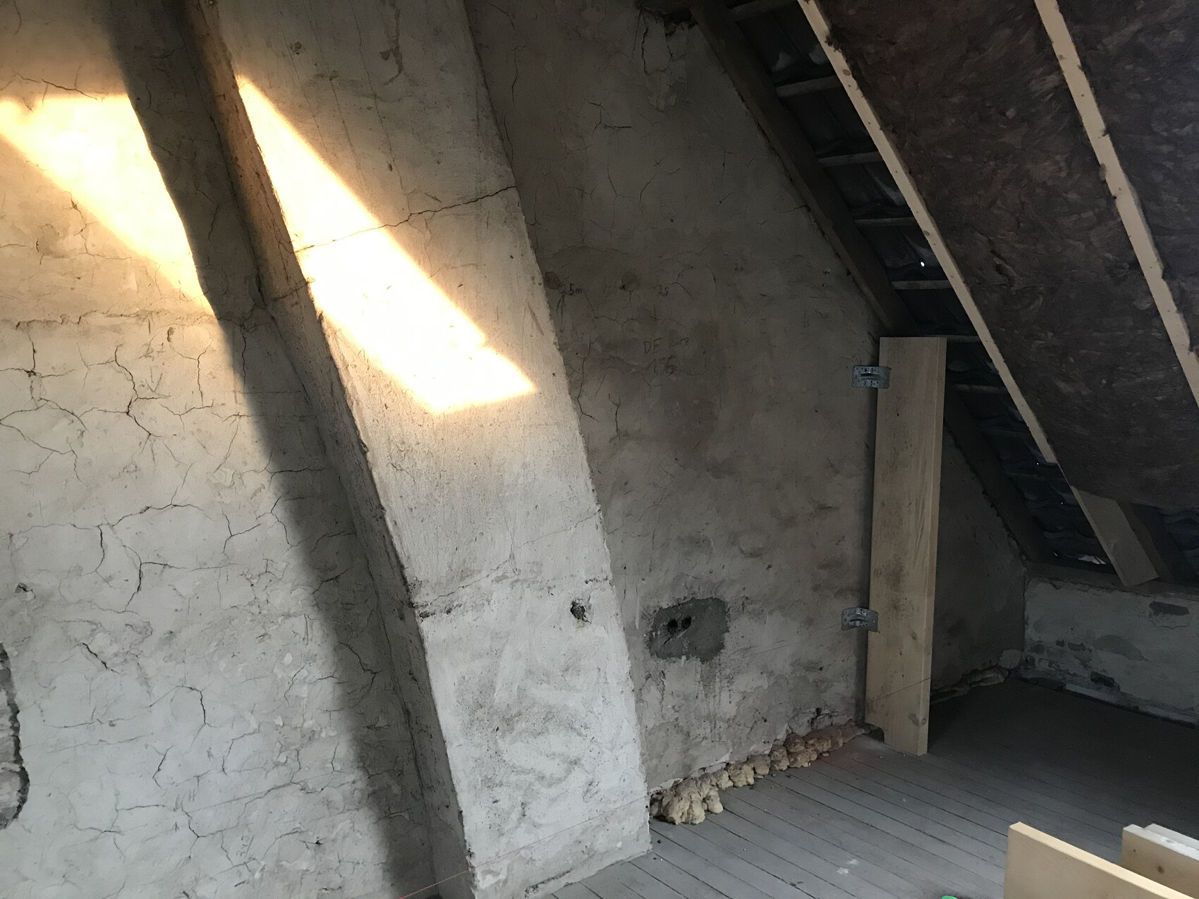 Attic with cracked wall, diagonal support pillar, wooden floor and beam of light through an opening.