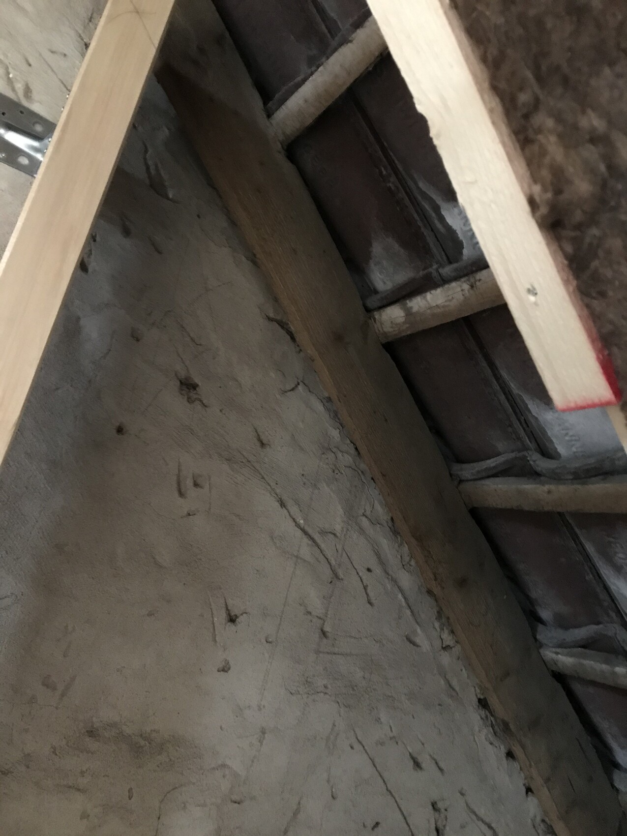 Attic shell with wooden beams, dusty wall and visible battens.