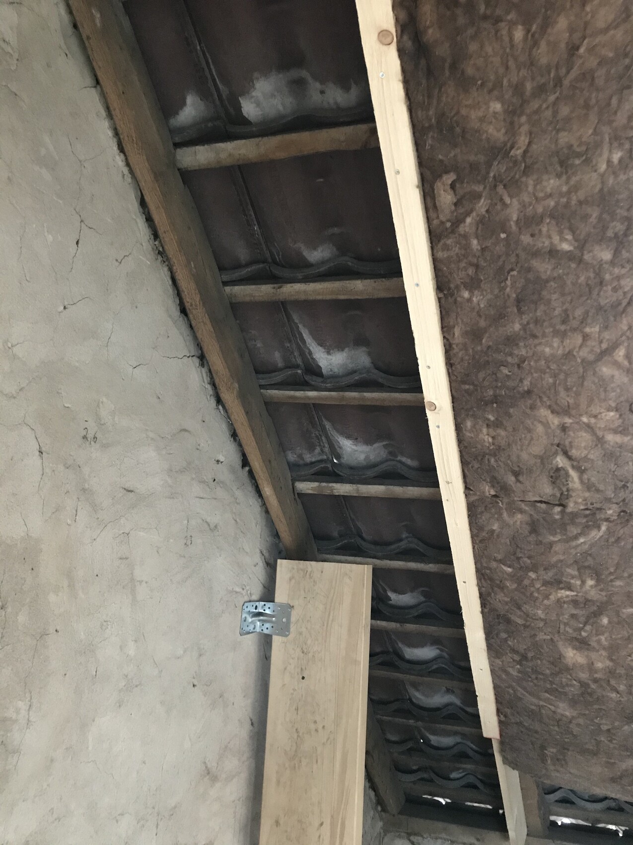 Attic view: wooden beams, roof tiles, insulation and a temporary wooden structure.