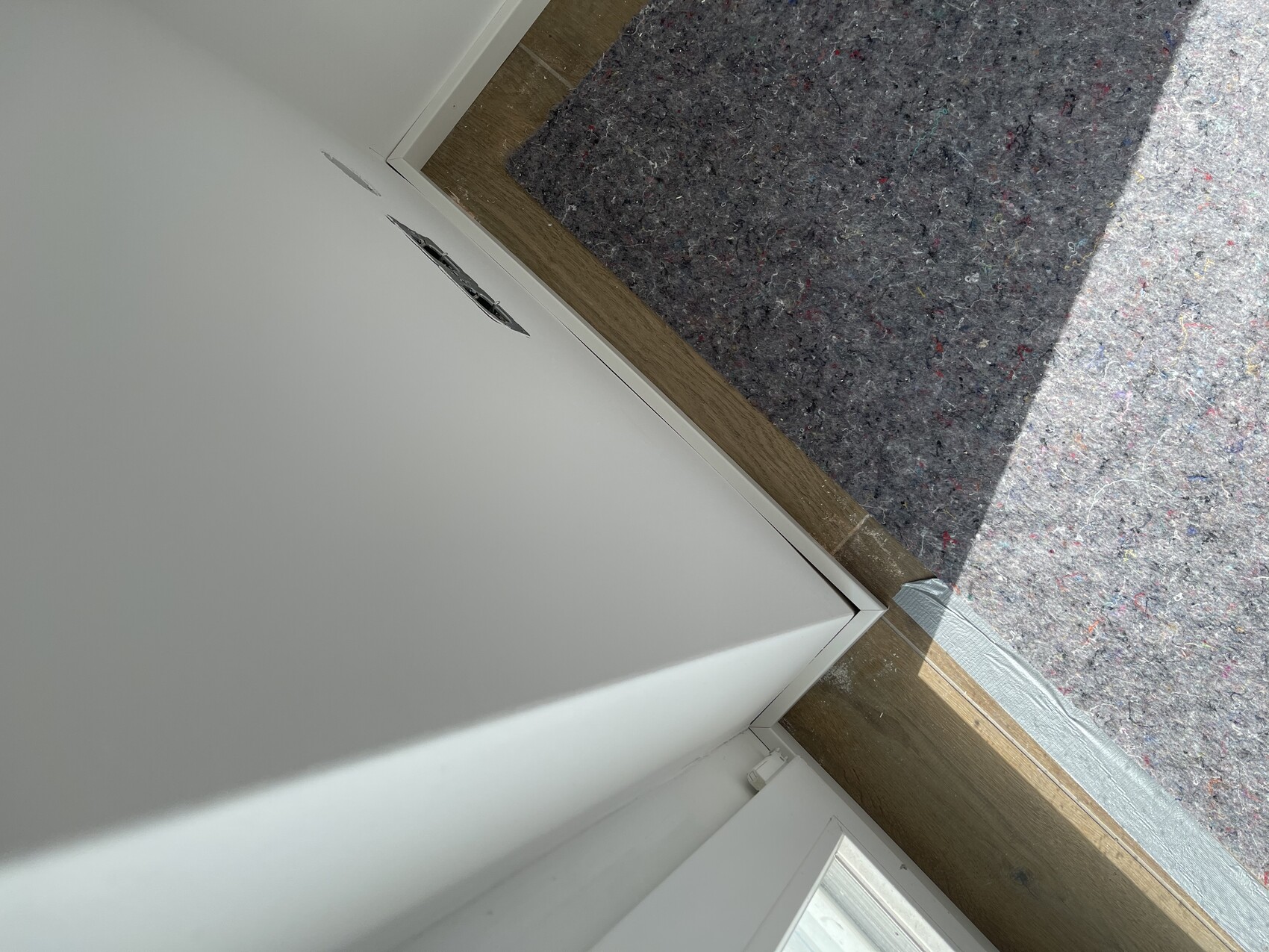 Türdurchgang: weiße Wand, Holzleiste, Türrahmen; grauer Außen-Teppich mit bunten Fasern.