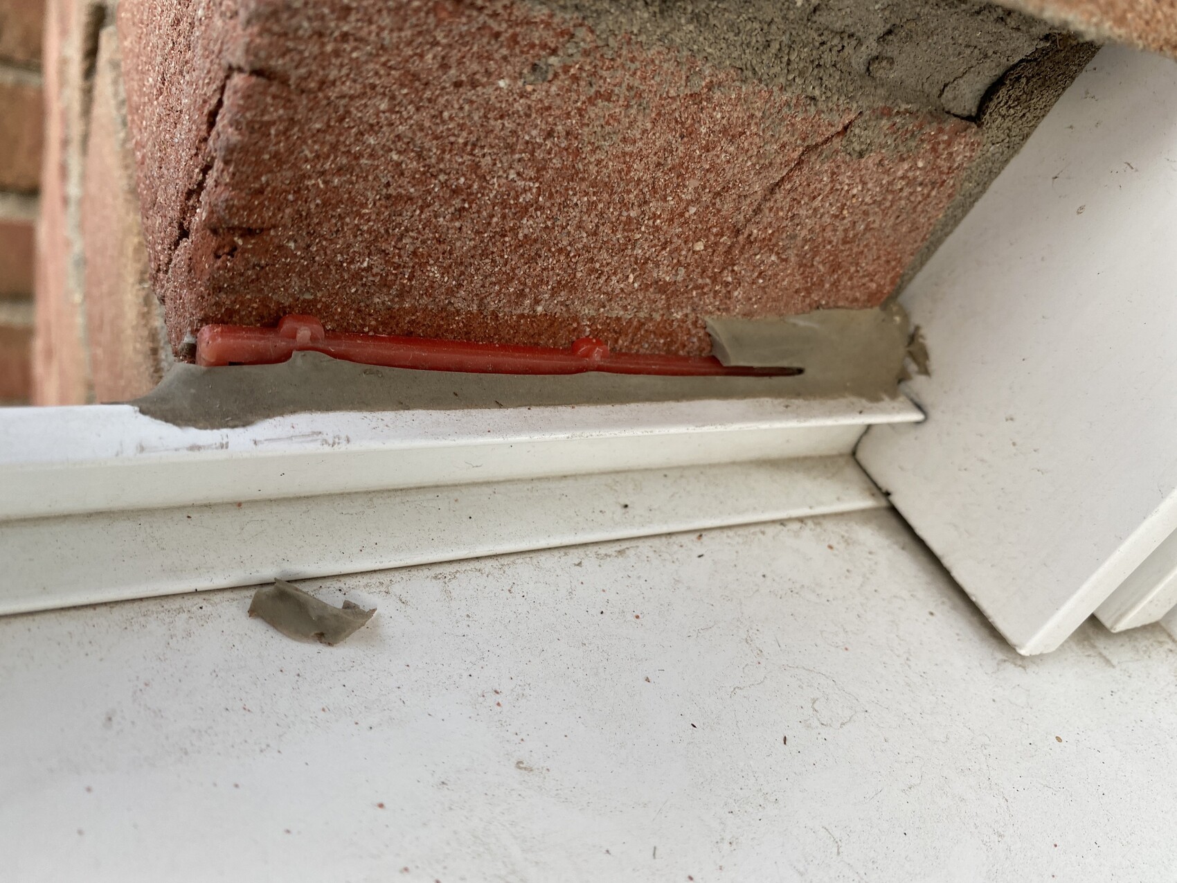 Roter Kabelbinder liegt im Spalt zwischen Ziegelwand und weißem Fenstersims.