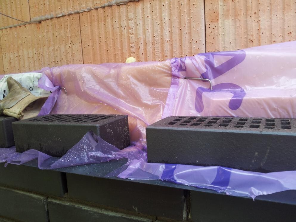 Construction site with black insulation boards, purple construction foil and stone wall in the background