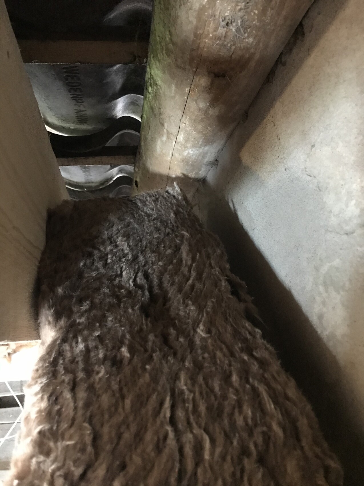 Large brown, fibrous insulation placed between wooden beams and wall in the attic.