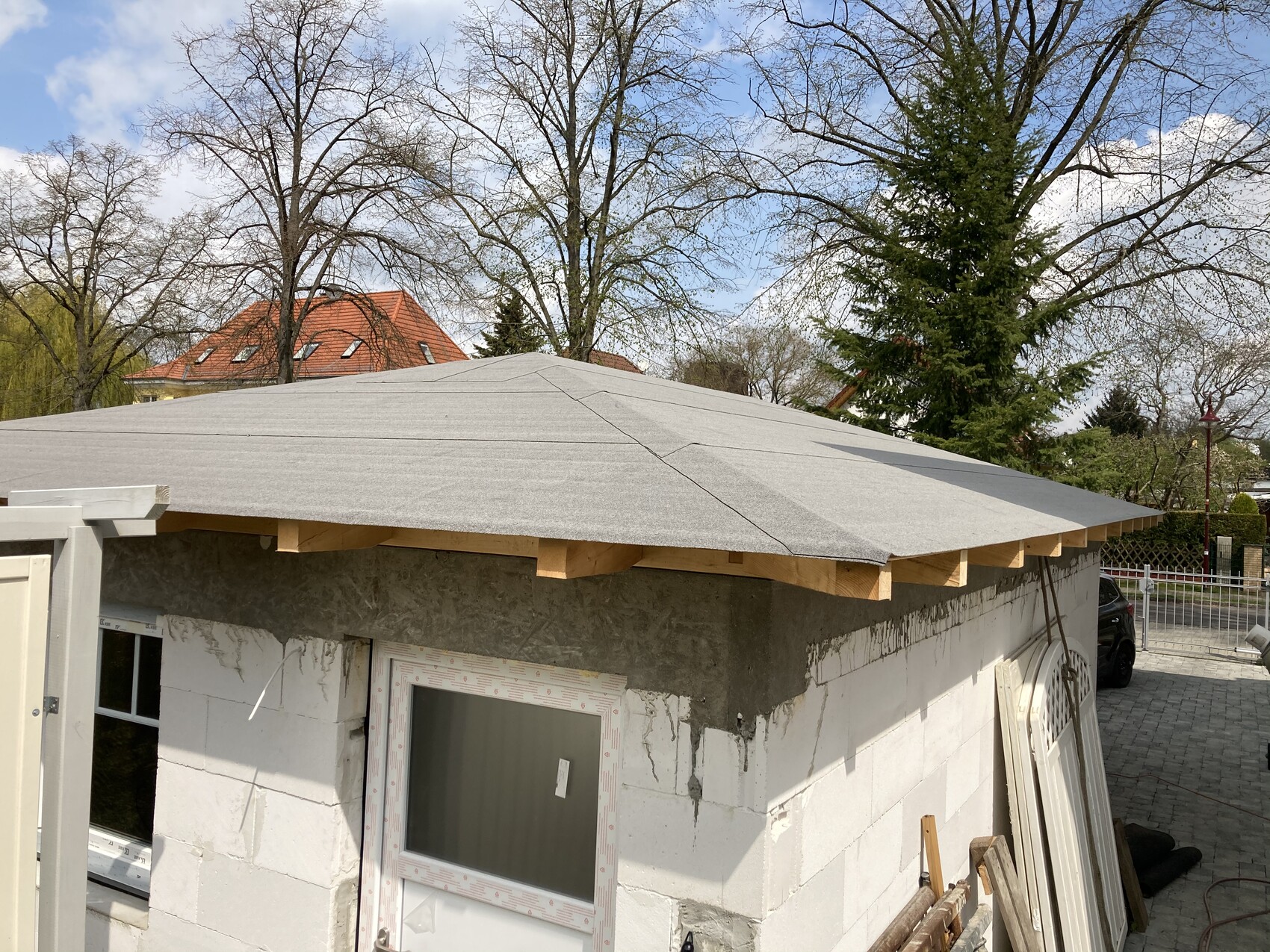 Kleines Bauprojekt-Häuschen mit neuem grauen Dach, sichtbarer Holzunterkonstruktion und Blockwänden.