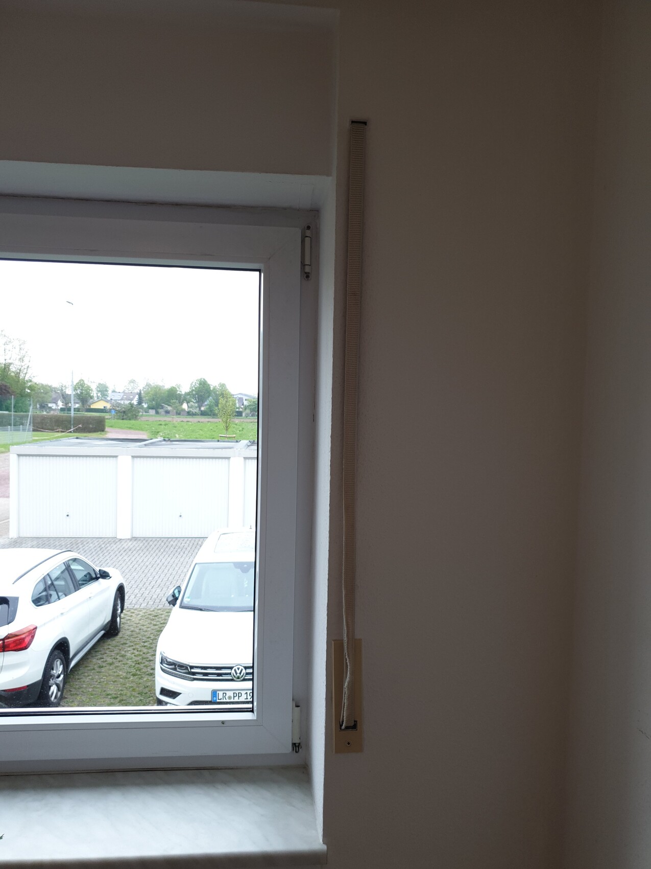 Interior view of a white window frame with a pull cord; parking spaces and garages outside.