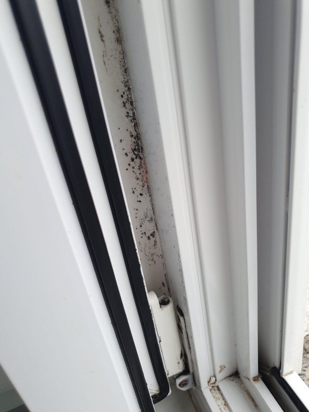 White window frame with dirty seals and rust stains on the edge.